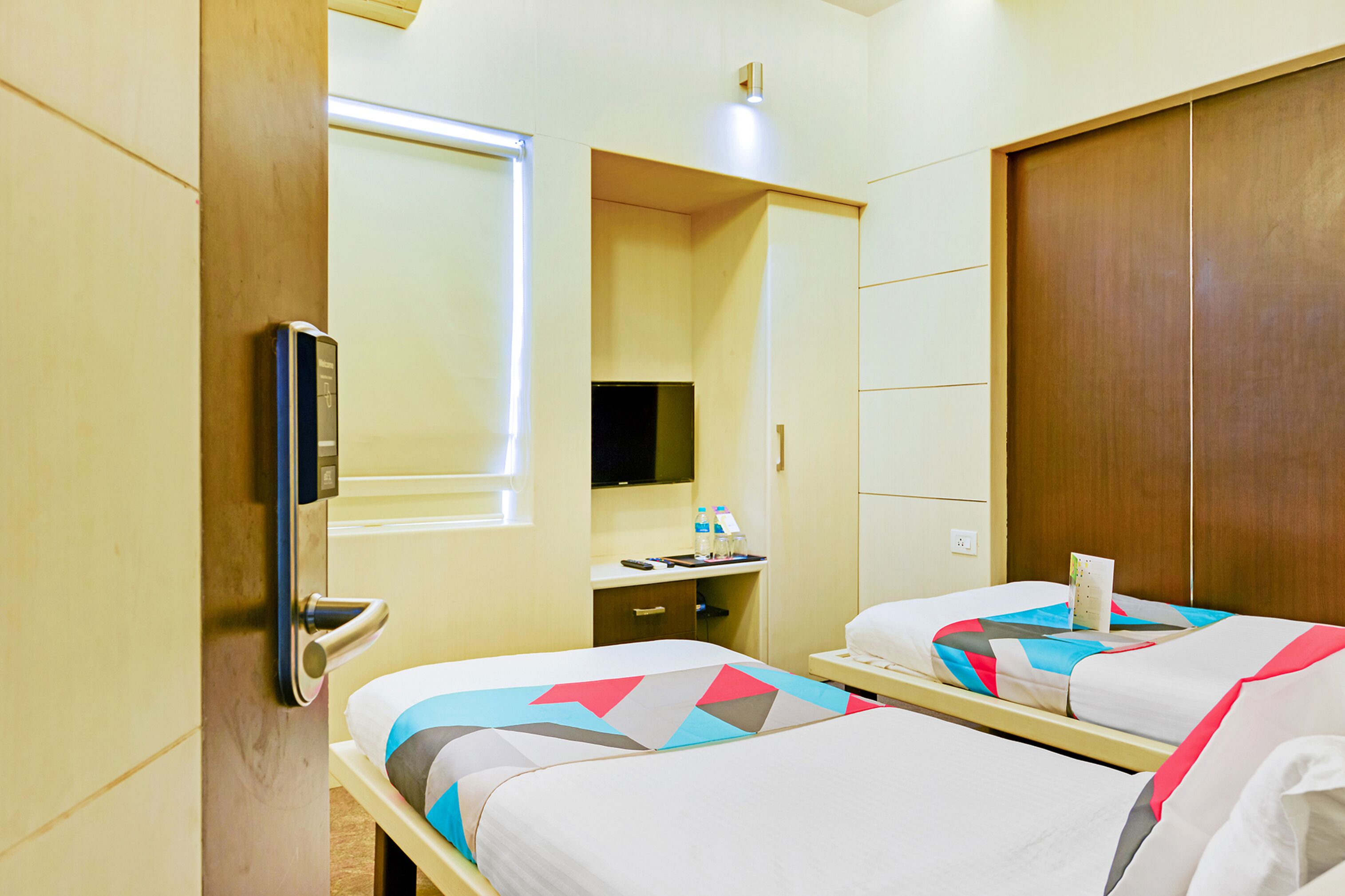 Une chambre d’hôtel avec deux lits, un bureau avec un miroir, une télévision et une armoire.