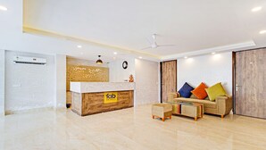 A hotel reception area with a wooden reception desk, a sofa with colorful cushions, and a glass coffee table. - Fabhotel Soft Petals (Gurugram)