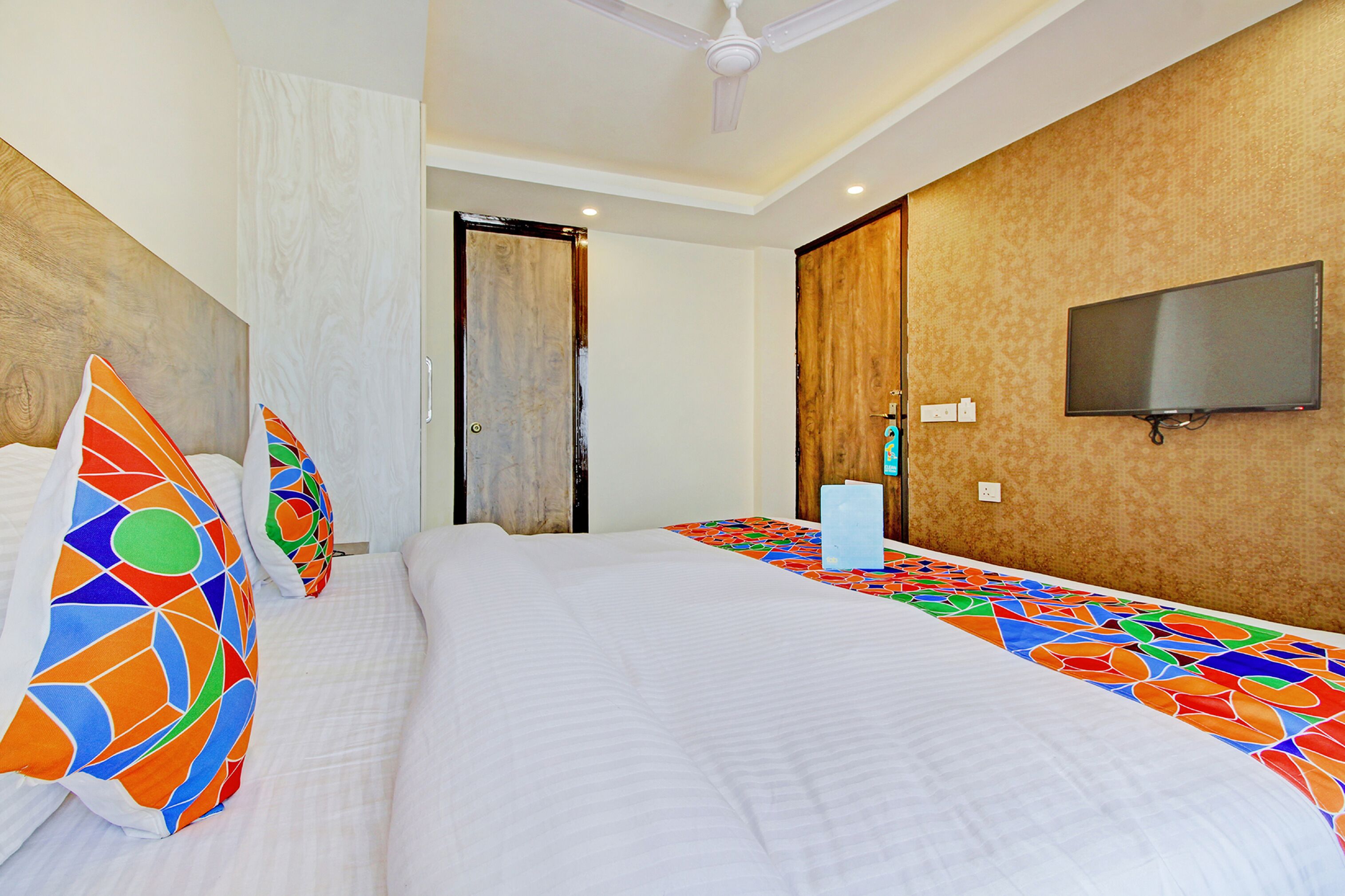Habitación de hotel con una cama grande, almohadas coloridas, un televisor de pantalla plana y un ventilador de techo.