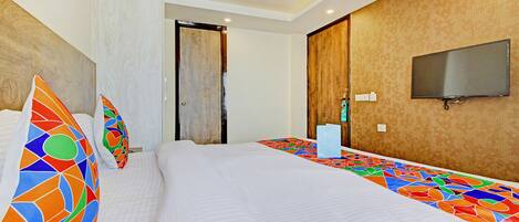 Habitación de hotel con una cama grande, almohadas coloridas, un televisor de pantalla plana y un ventilador de techo.