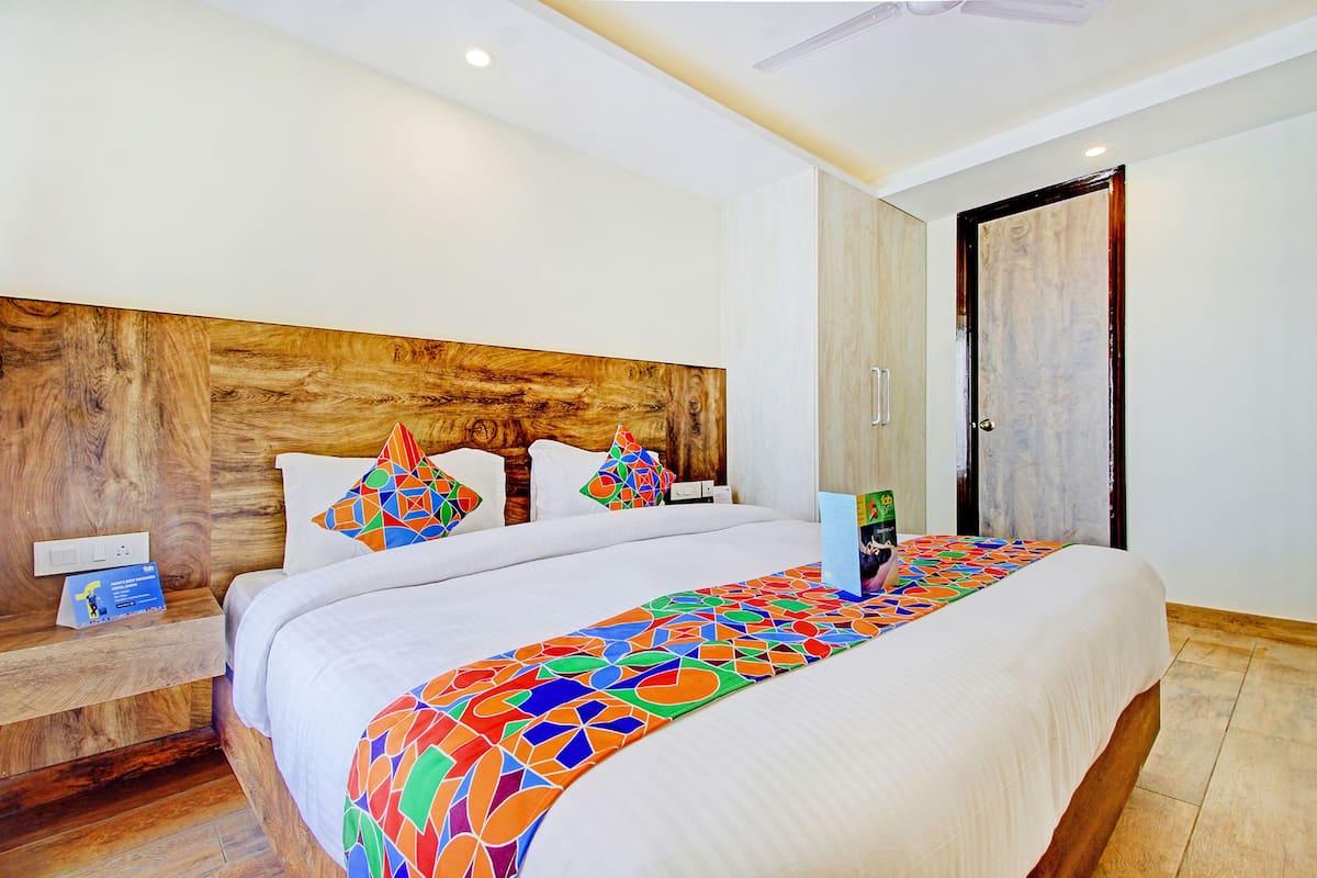 A hotel room with a wooden headboard, a large bed with colorful bedding, a nightstand with a book, and a door with a marble panel.