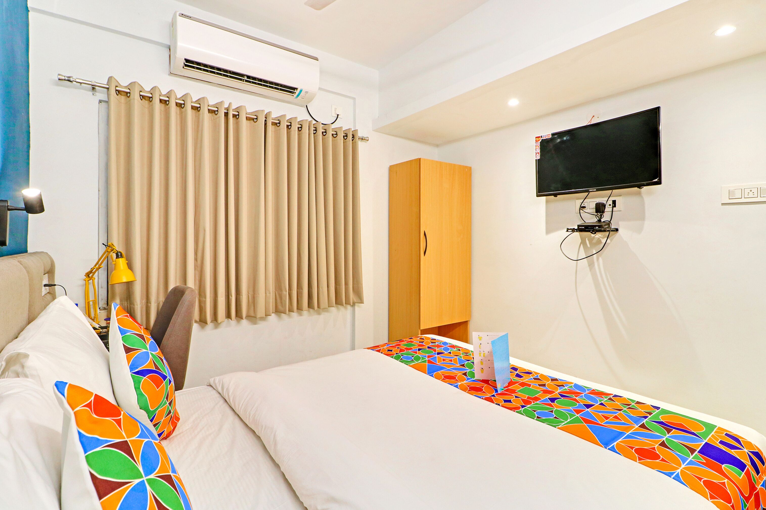 A hotel room with a bed, a TV mounted on the wall, an air conditioner, and a wardrobe.
