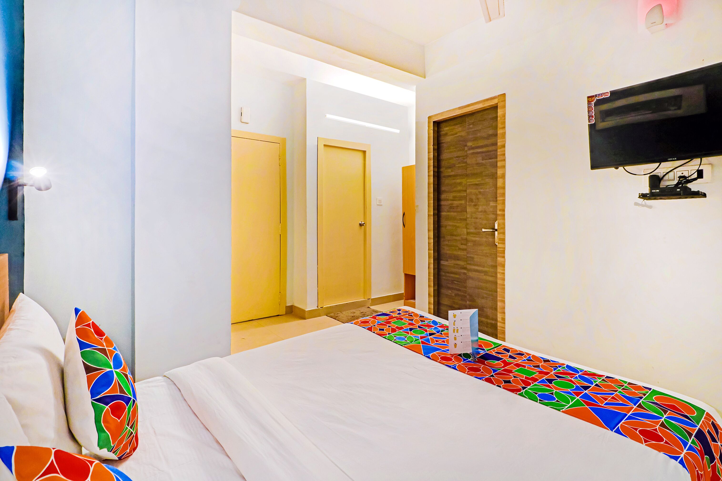 Een hotelkamer met een bed, een aan de muur bevestigde televisie en een deur die naar een andere kamer leidt.
