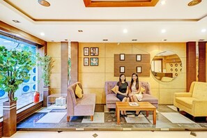 A modern lobby with a reception desk, two sofas, a coffee table, and a large mirror. - FabHotel Azure Sky (Kolkata)