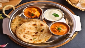 Un plato de acero inoxidable con pan naan, dos tipos de curry y un pequeño cuenco de yogur.