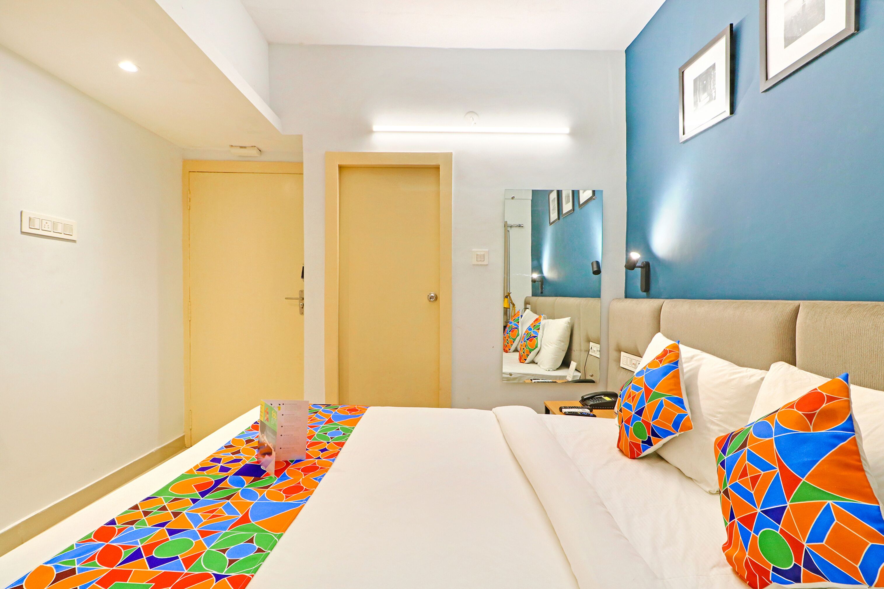 A hotel room with a bed, a bedside table, a mirror, and a door.