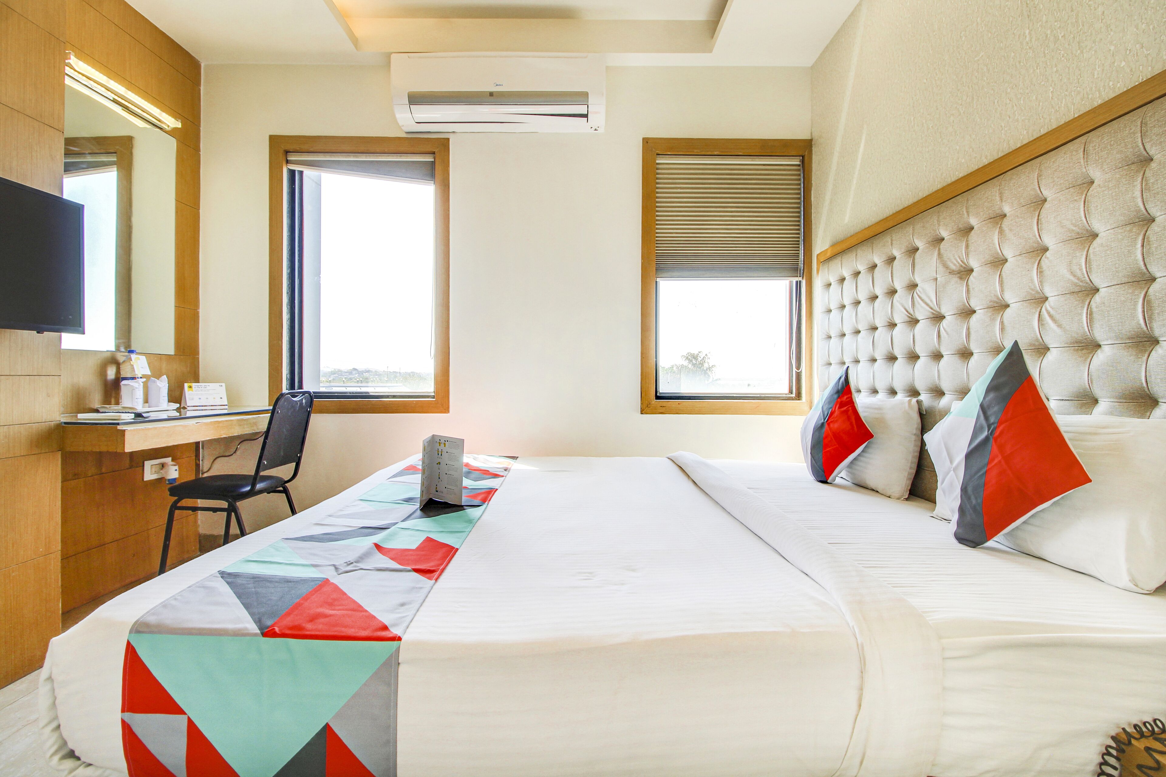 A hotel room with a bed, a desk, a chair, a television, and a window.