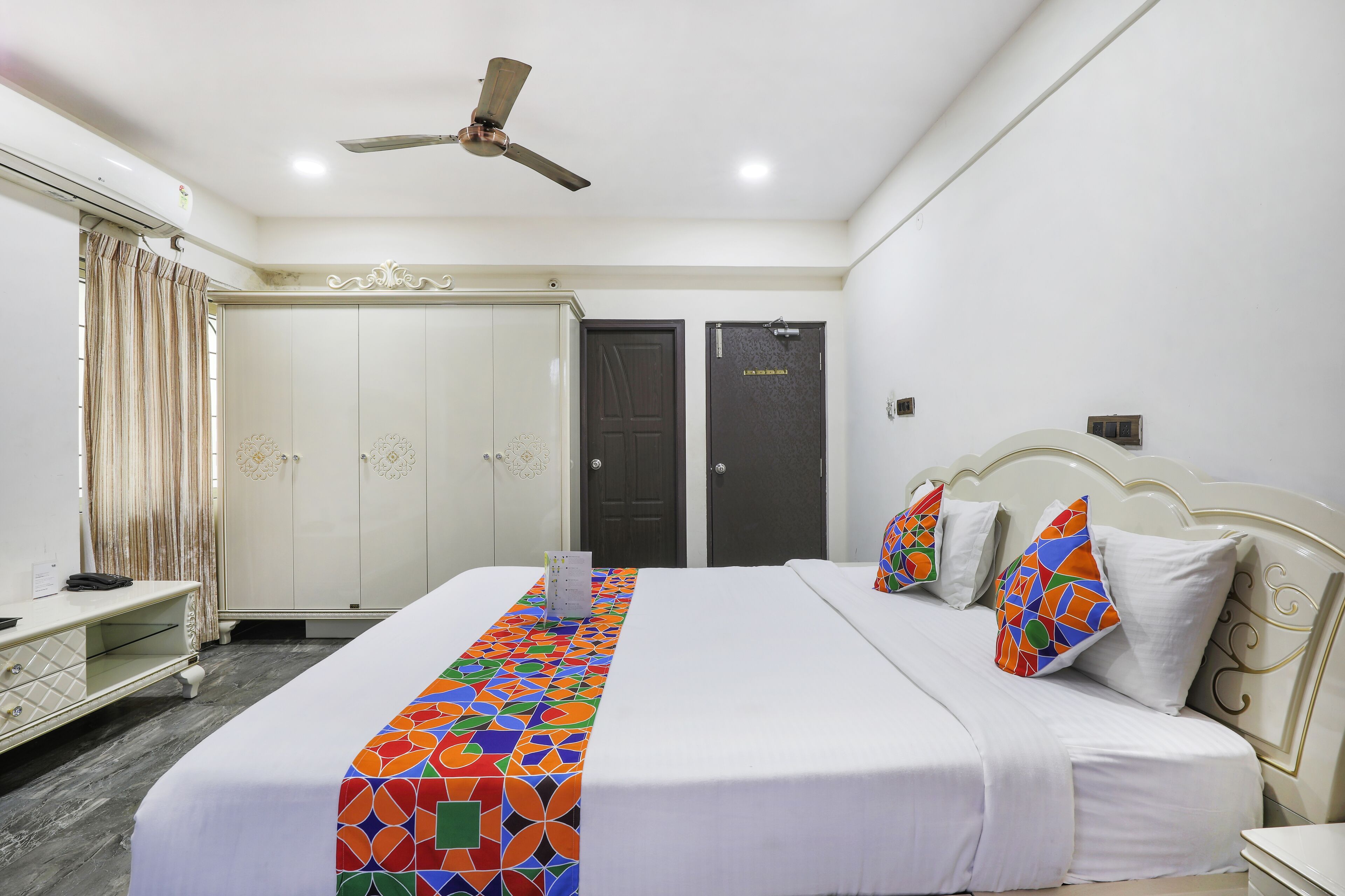Une chambre d’hôtel avec un lit, un ventilateur de plafond, une armoire et une porte.
