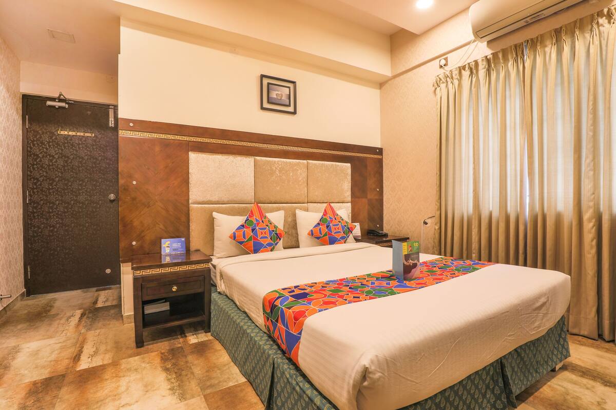 A hotel room with a bed, a nightstand, a dresser, a door, and a window with curtains.