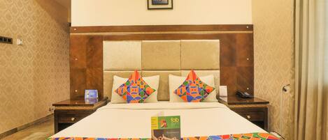 A hotel room with a large bed, a wooden headboard, two nightstands, a framed picture on the wall, and a colorful bedspread.