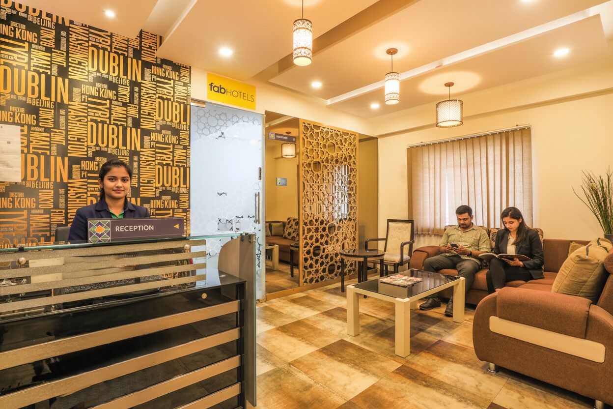 A hotel reception area with a reception desk, a seating area with sofas and a coffee table, and a decorative wall with city names.