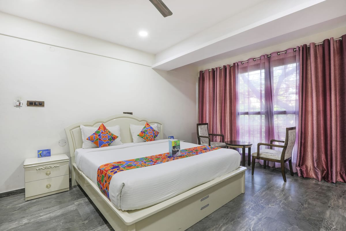 A hotel room with a bed, bedside table, chair, and curtains.