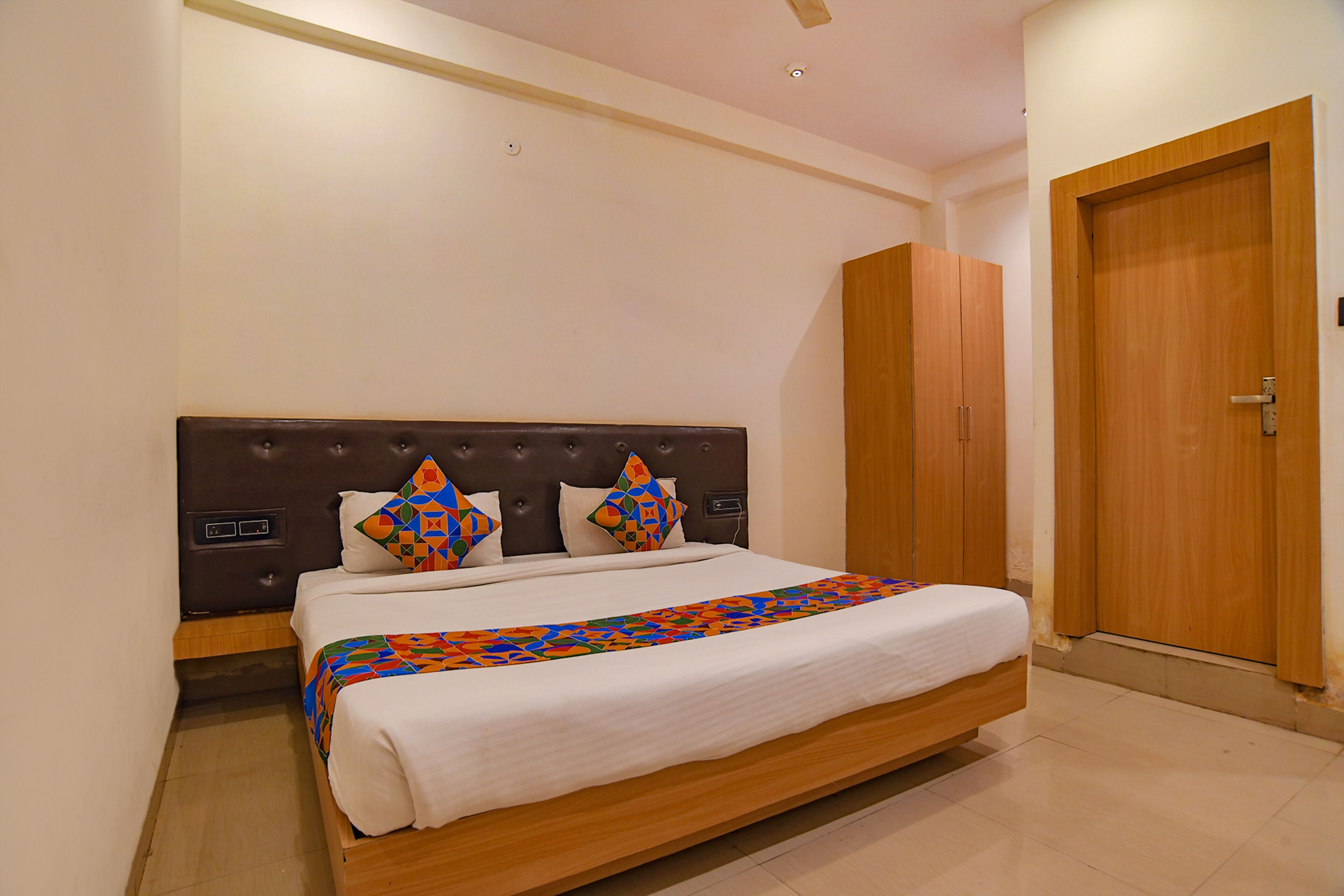 A neatly made bed with a patterned bedspread, a headboard with a control panel, and a wooden wardrobe.