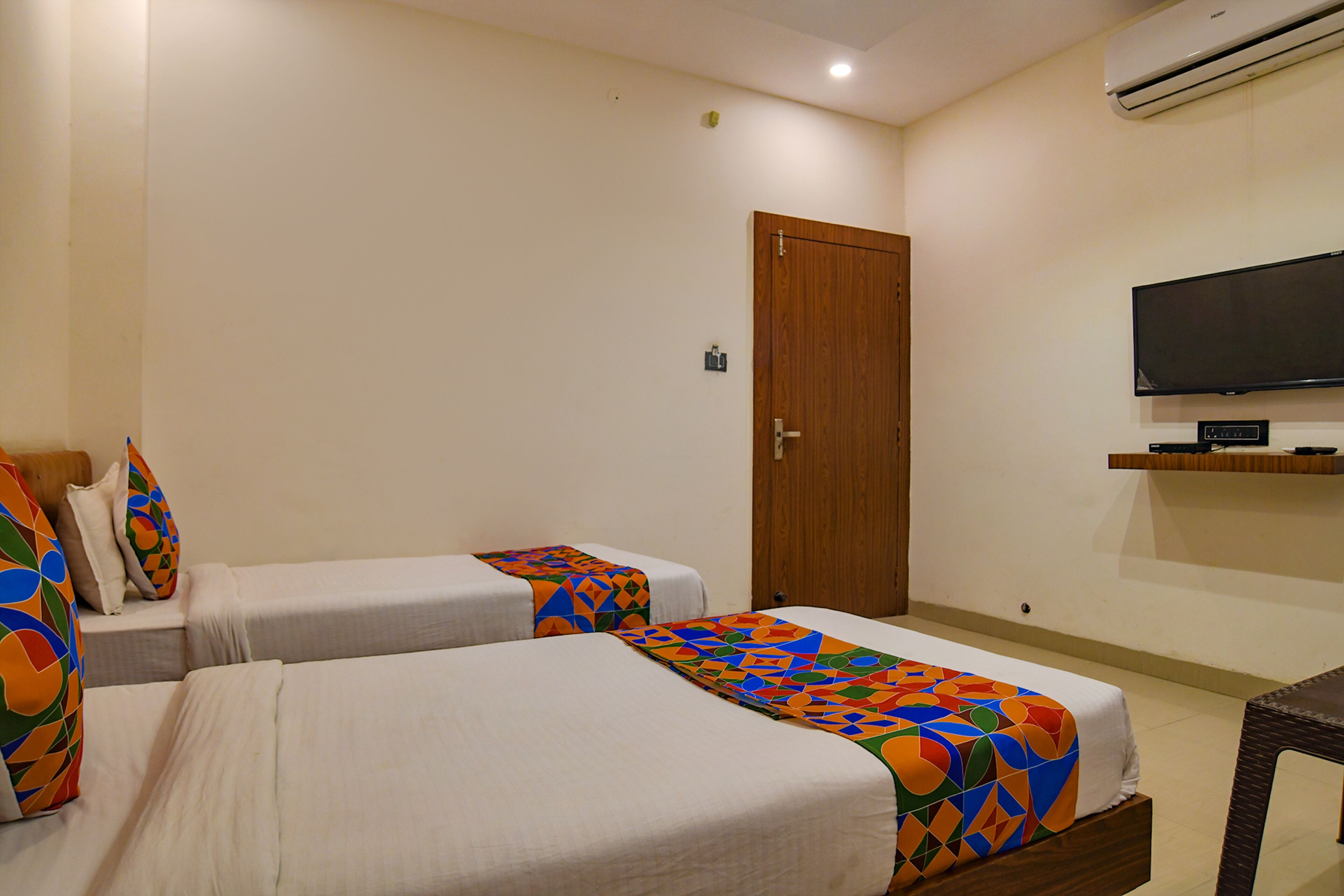 A hotel room with two beds, a television, and an air conditioning unit.