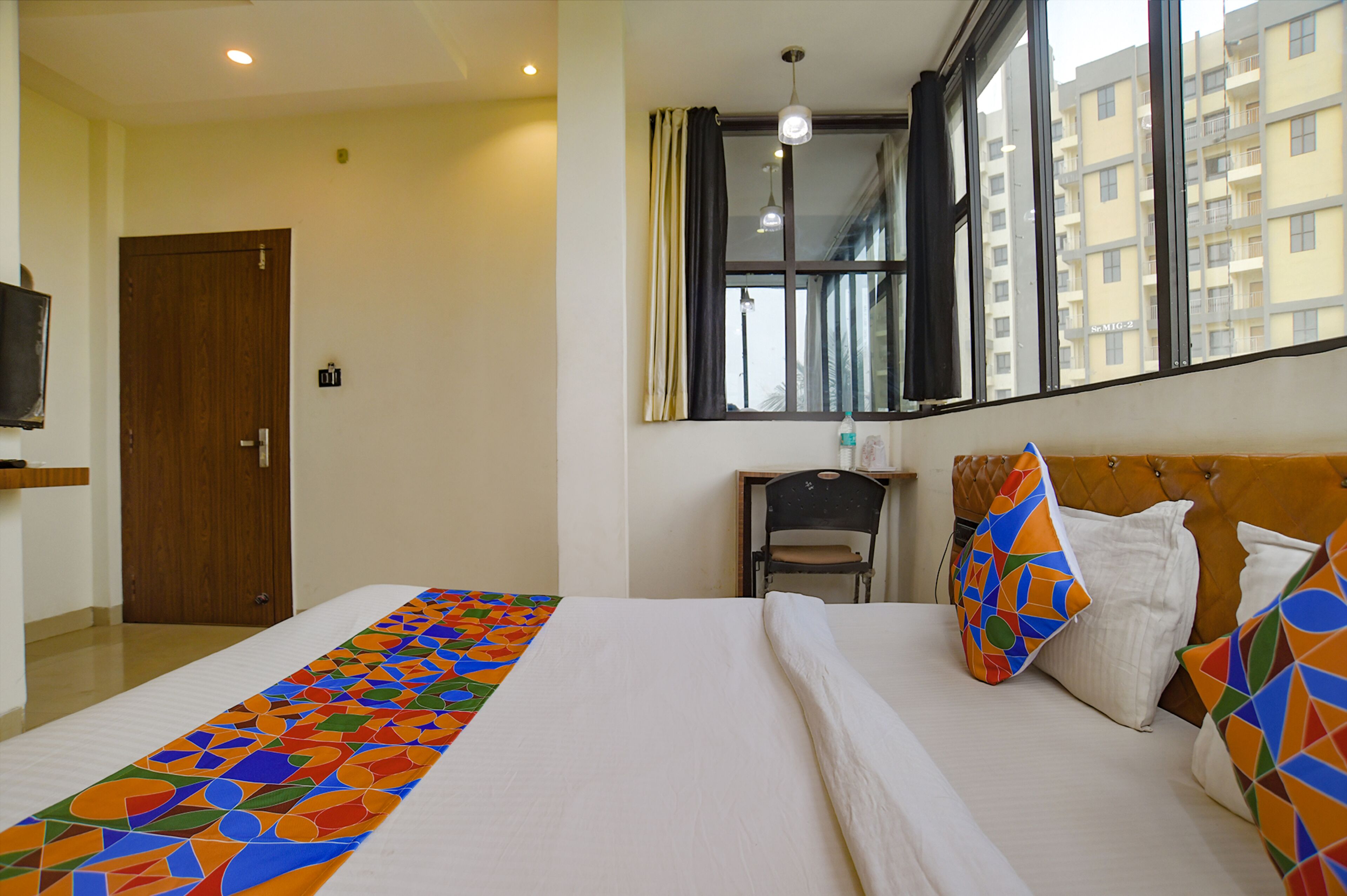 Quarto de hotel com cama grande, uma cadeira, televisão e janela com vista para edifícios.