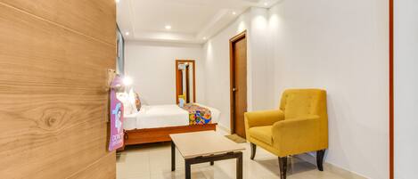 A hotel room with a bed, a small table, a yellow armchair, and a wooden accent wall.