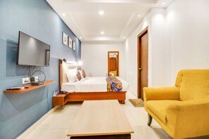 A modern hotel room with a bed, a TV mounted on the wall, a yellow armchair, and a small table.