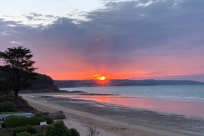 Sonnenuntergang am Meer mit Strand, Baum und Haus.