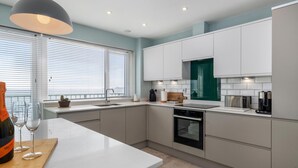 Eine moderne Küche mit weißen Schränken, einem eingebauten Backofen und einem großen Fenster mit Jalousien.