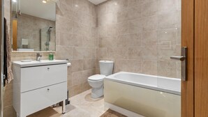 A modern bathroom with a white vanity, a glass shower enclosure, and a beige-tiled wall. - Dolphins Apartment - Spectacular Sea Views (Saundersfoot)