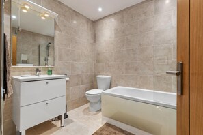 A modern bathroom with a white vanity, a glass shower enclosure, and a beige-tiled wall. - Dolphins Apartment - Spectacular Sea Views (Saundersfoot)