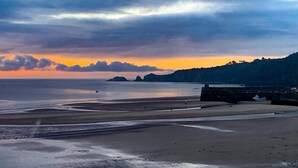 A coastal landscape with a beach, calm sea, and distant hills. - Dolphins Apartment - Spectacular Sea Views (Saundersfoot)