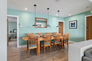 A dining area with a wooden table and chairs, a large mirror above, and pendant lights. - Dolphins Apartment - Spectacular Sea Views (Saundersfoot)
