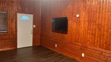 A room with wooden paneling, a white door with a blue window, and a mounted flat-screen TV.