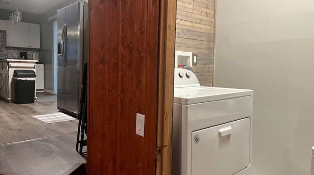 Une cuisine équipée d’un réfrigérateur en acier inoxydable, d’un lave-linge blanc et d’une porte en bois.