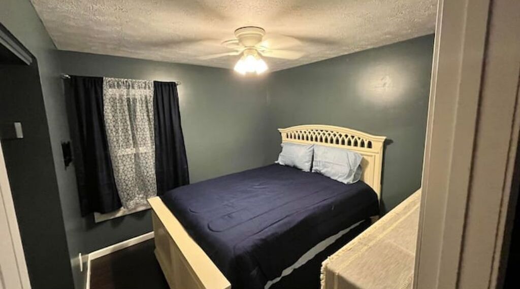 A single bed with a headboard, a ceiling fan, and a window with curtains.