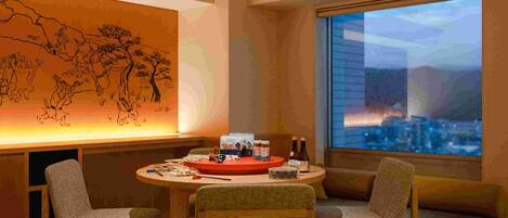 Ein modernes Zimmer mit einem runden Tisch, zwei Stühlen, einem großen Fenster mit Stadtblick und einer Wand mit traditioneller Kunst.