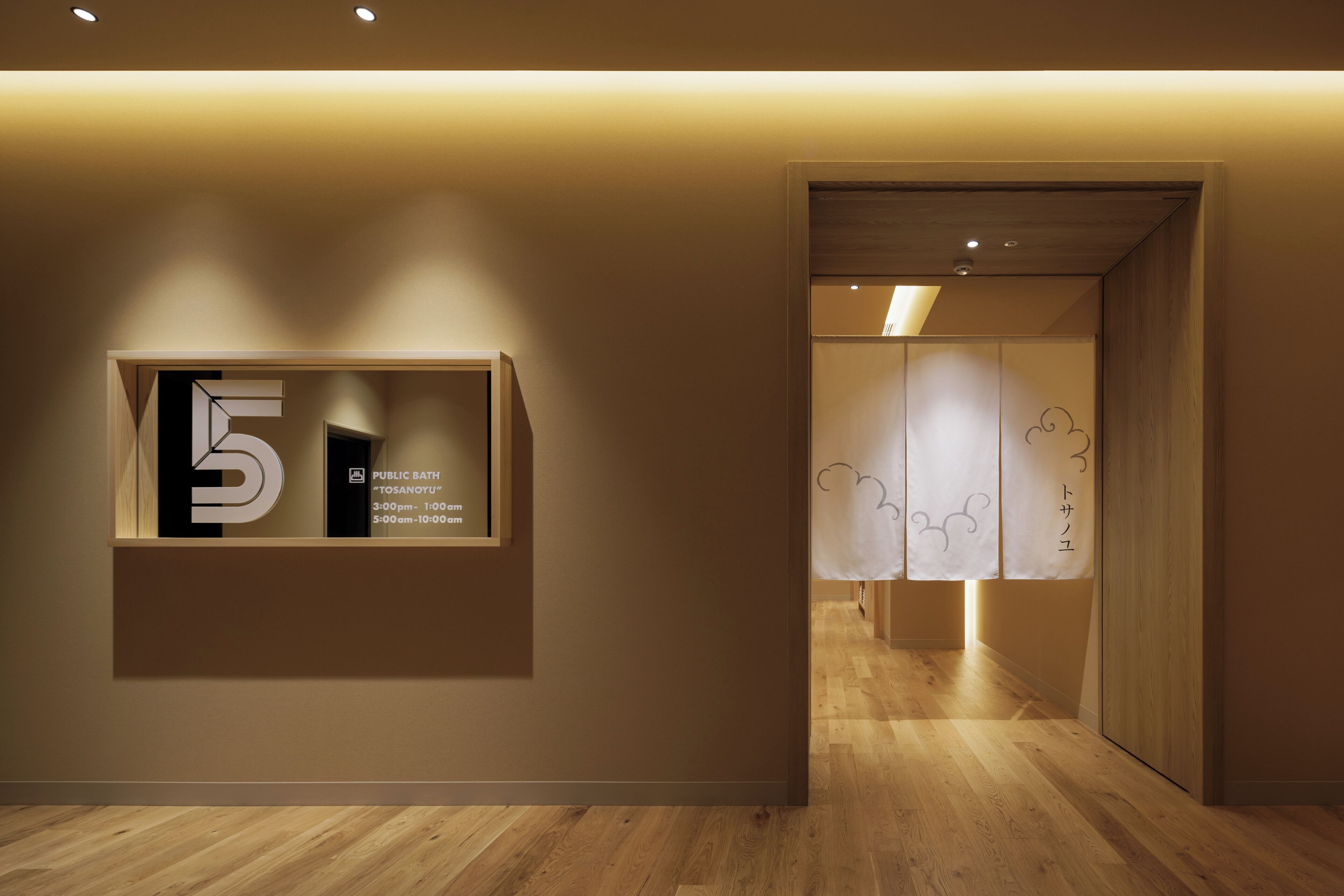 A hallway with a wooden floor, a wall-mounted sign indicating a public bath, and a door leading to another room.