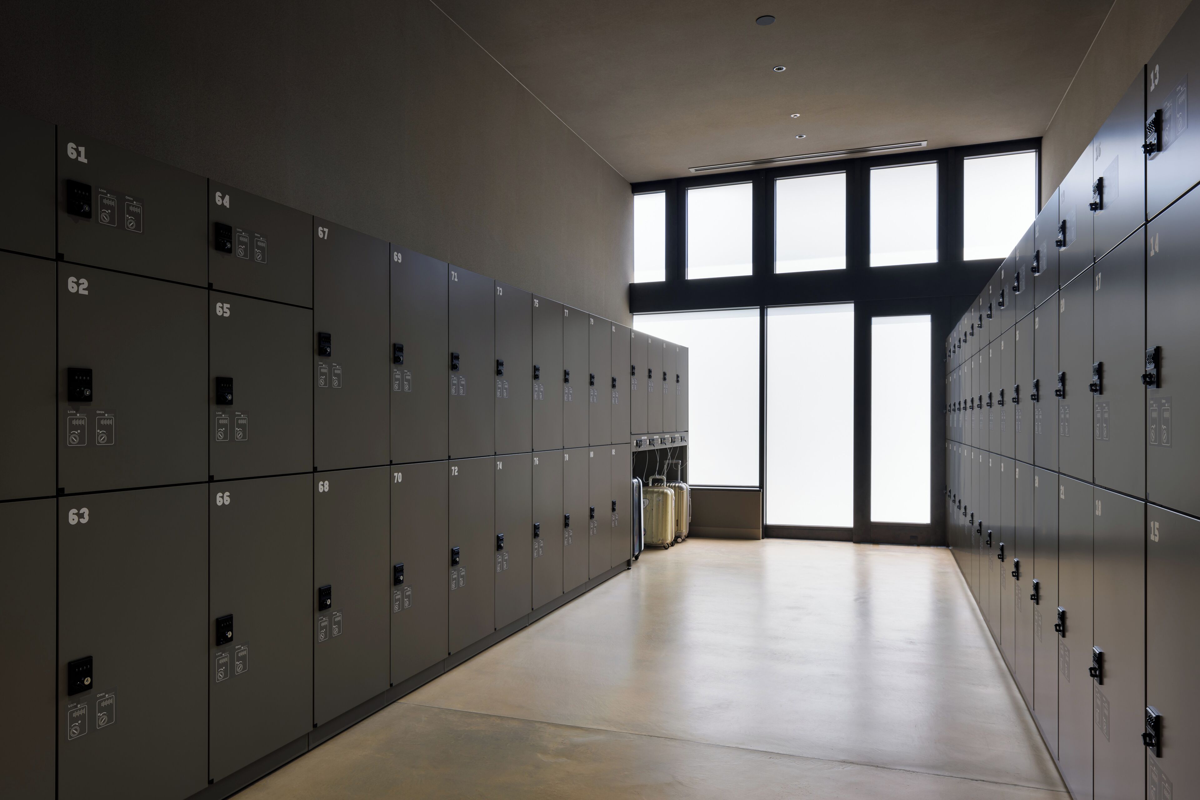 Eine Reihe grauer Schließfächer mit Nummern und Symbolen, ein heller Boden und große Fenster, die natürliches Licht hereinlassen.