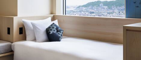 A modern hotel room with a wooden headboard, a white bed, and a city view through large windows.