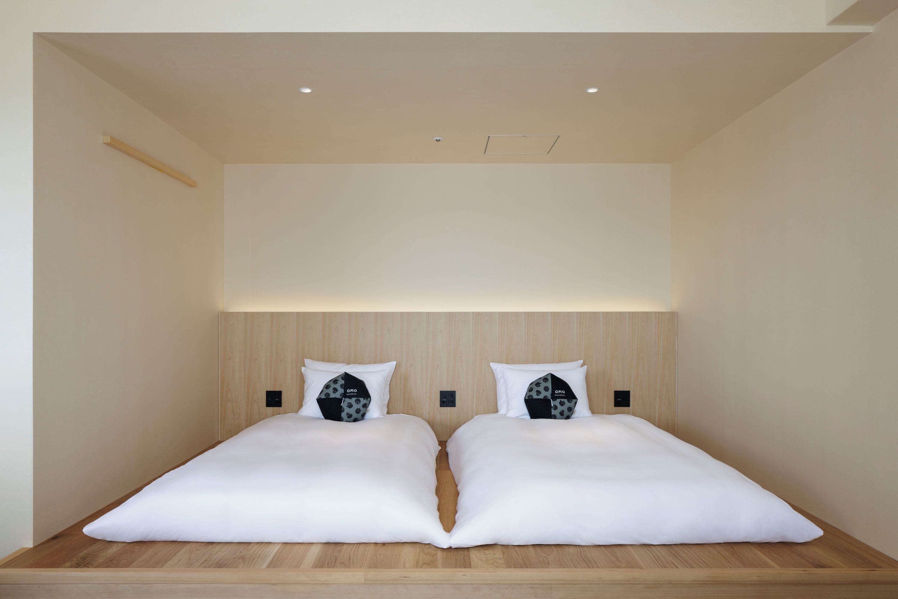 A modern bedroom with a wooden headboard, two beds with white bedding, and a light-colored ceiling.