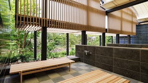 A modern outdoor seating area with wooden benches, a stone wall, and a view of greenery. - OMO7 Kochi by Hoshino Resorts (Kochi)