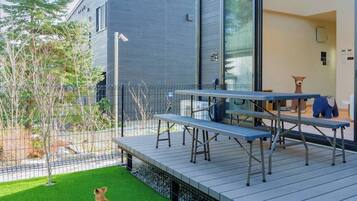 Un patio exterior moderno con una mesa y bancos de metal, rodeado por una cerca metálica y un pequeño césped.