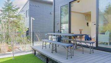 A modern outdoor deck with a metal table and benches, surrounded by a metal fence and a small lawn.