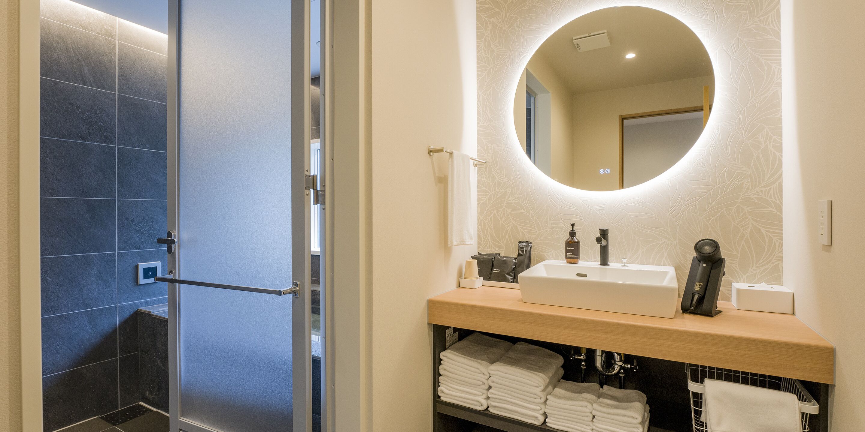 A modern bathroom with a glass shower door, a sink with a mirror above, and neatly folded towels on a shelf.