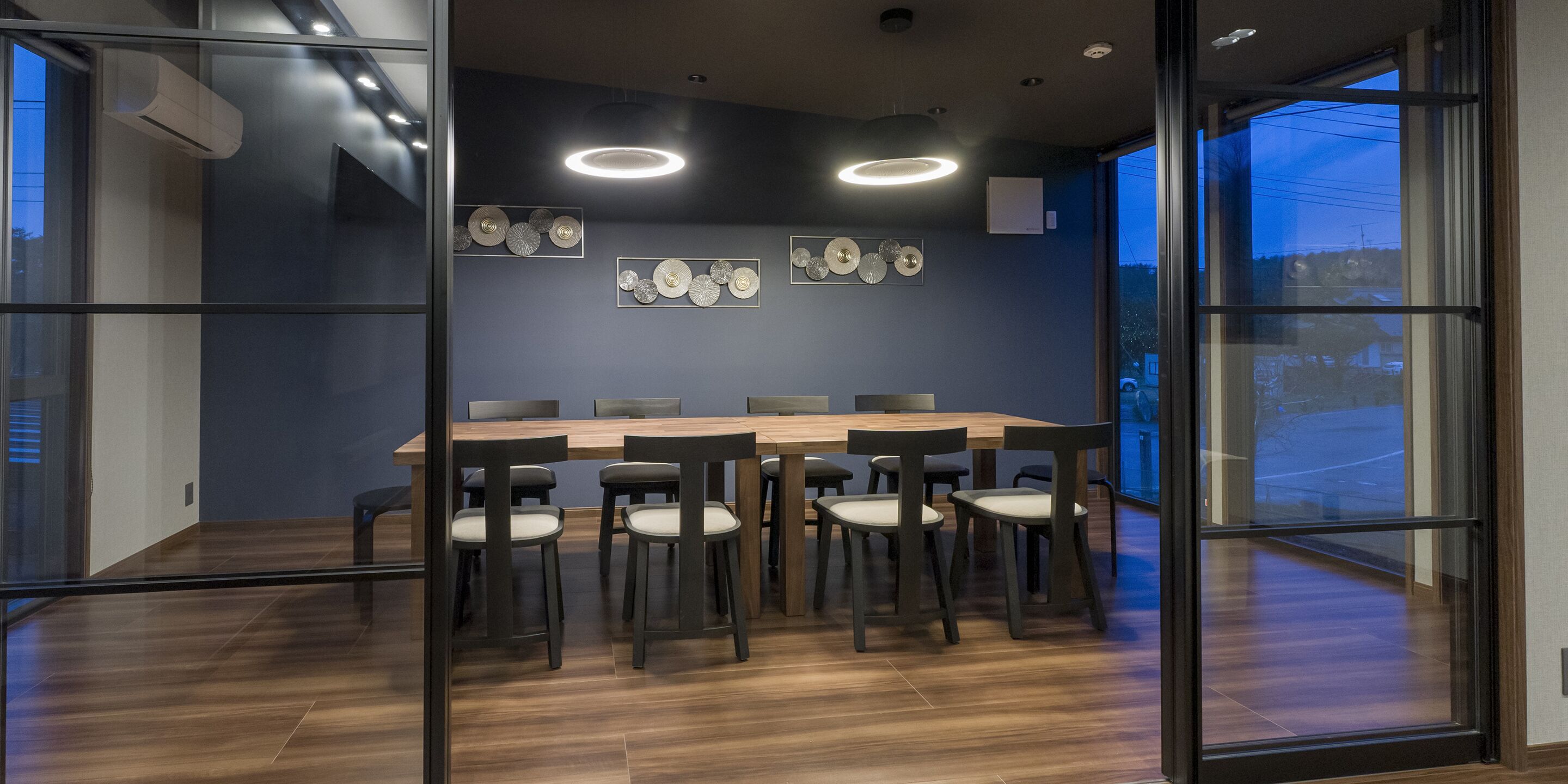 Una sala de conferencias moderna con una gran mesa de madera, sillas negras y elementos decorativos en la pared.