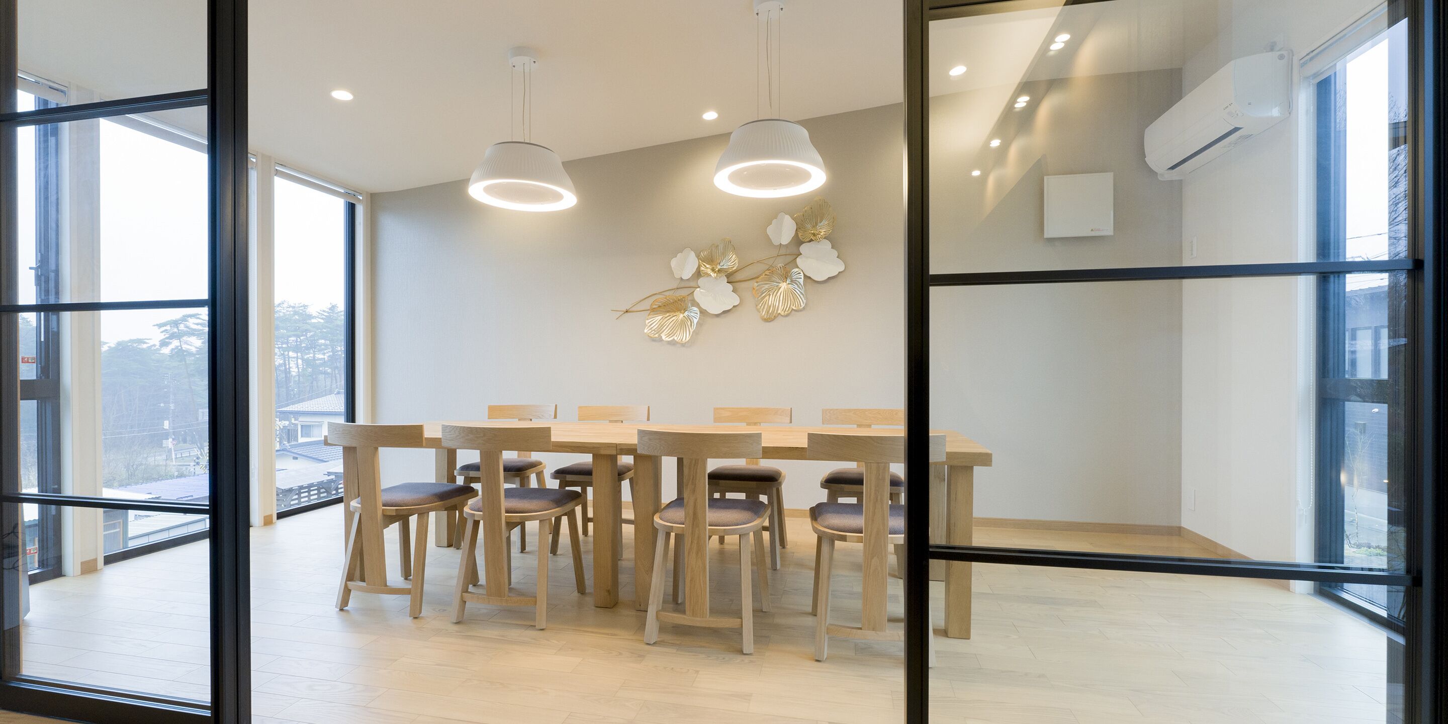 Un comedor moderno con una mesa y sillas de madera, ventanas amplias y un adorno en la pared.