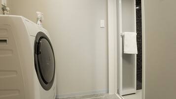 A laundry area with a front-loading washing machine, a bottle of detergent, and a towel rack.