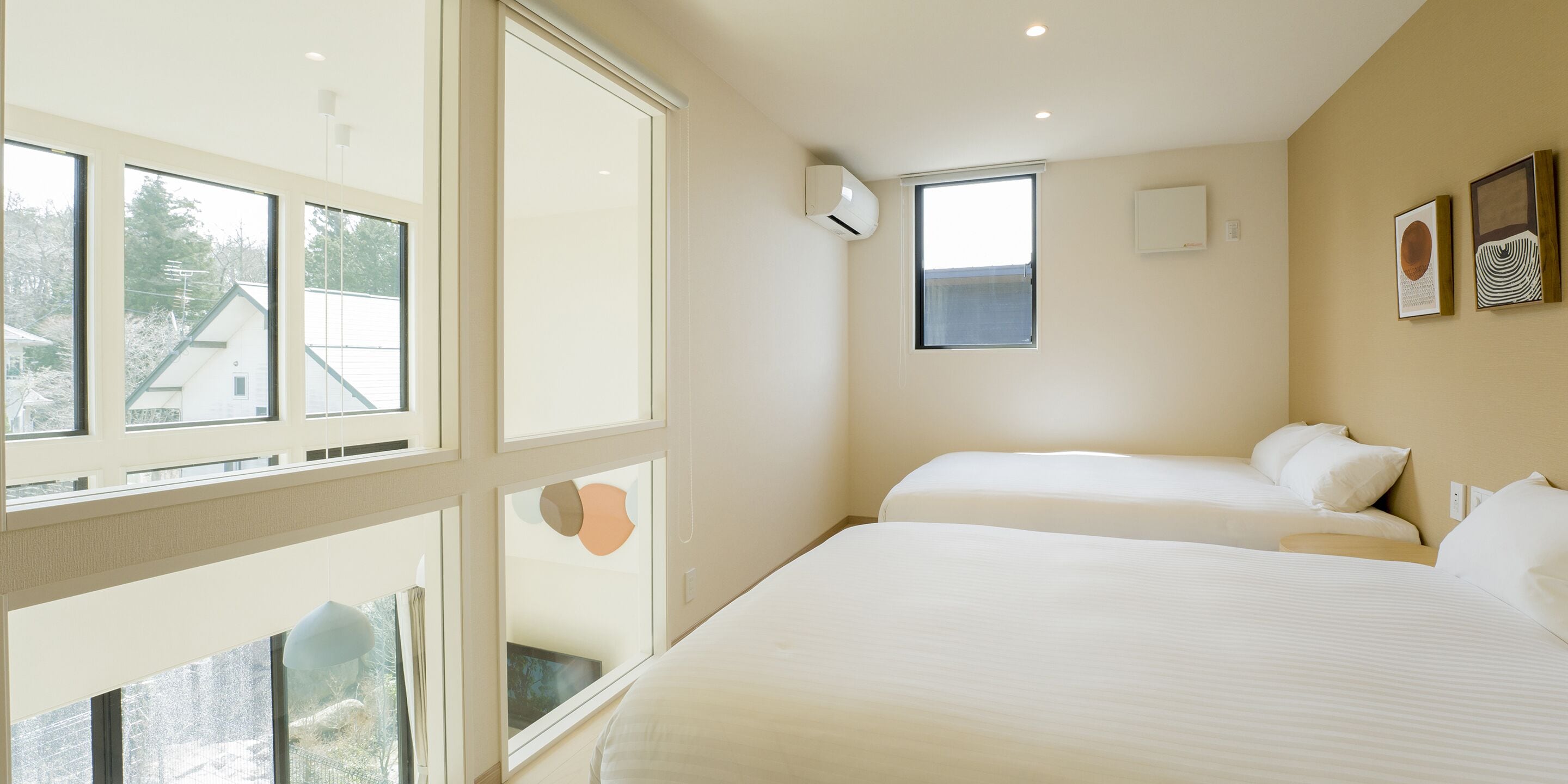 A modern hotel room with large windows, a bed, a bedside table, and a wall-mounted air conditioner.