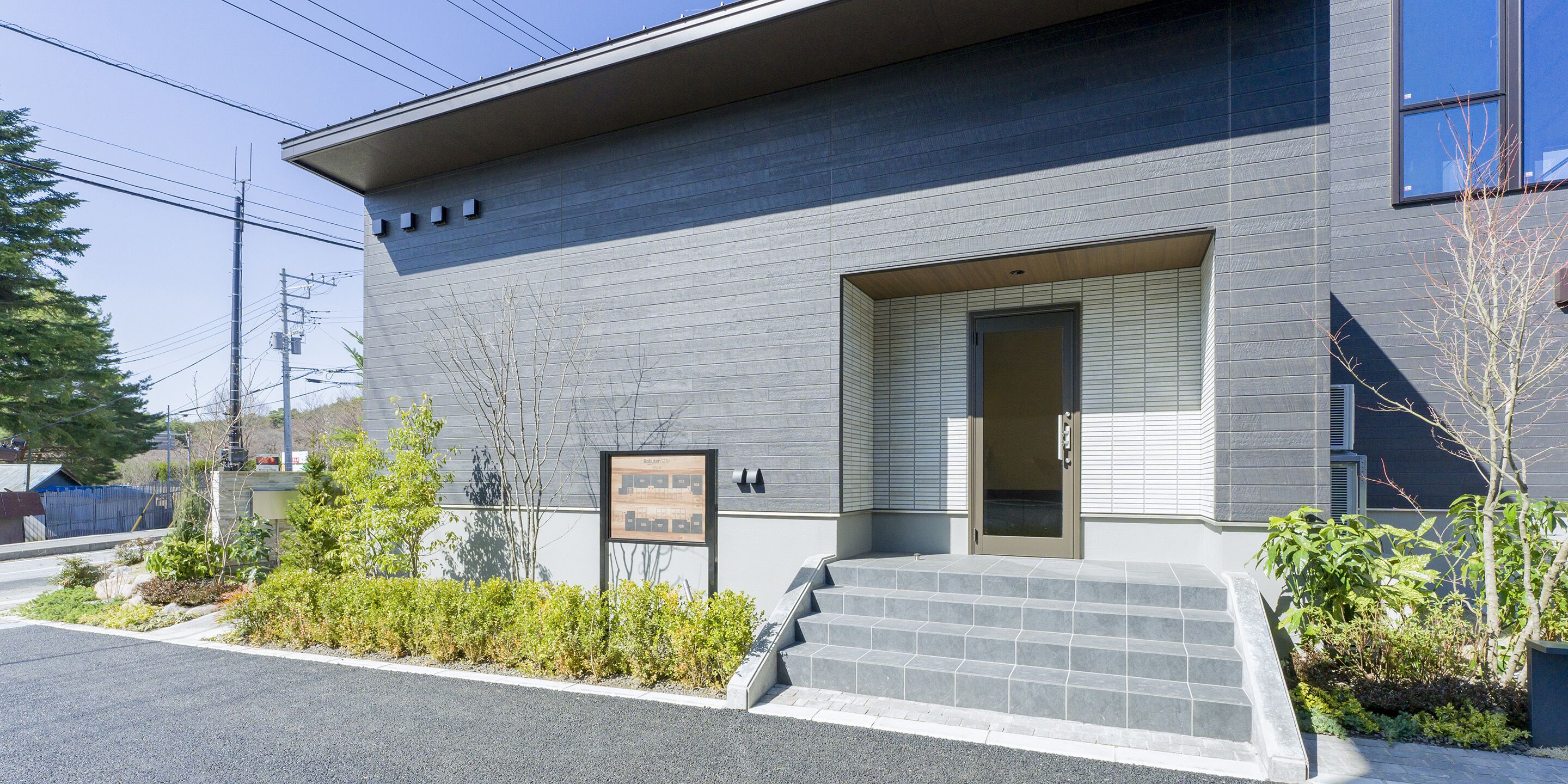 A modern building with a grey facade, a small entrance with steps, and a signboard.