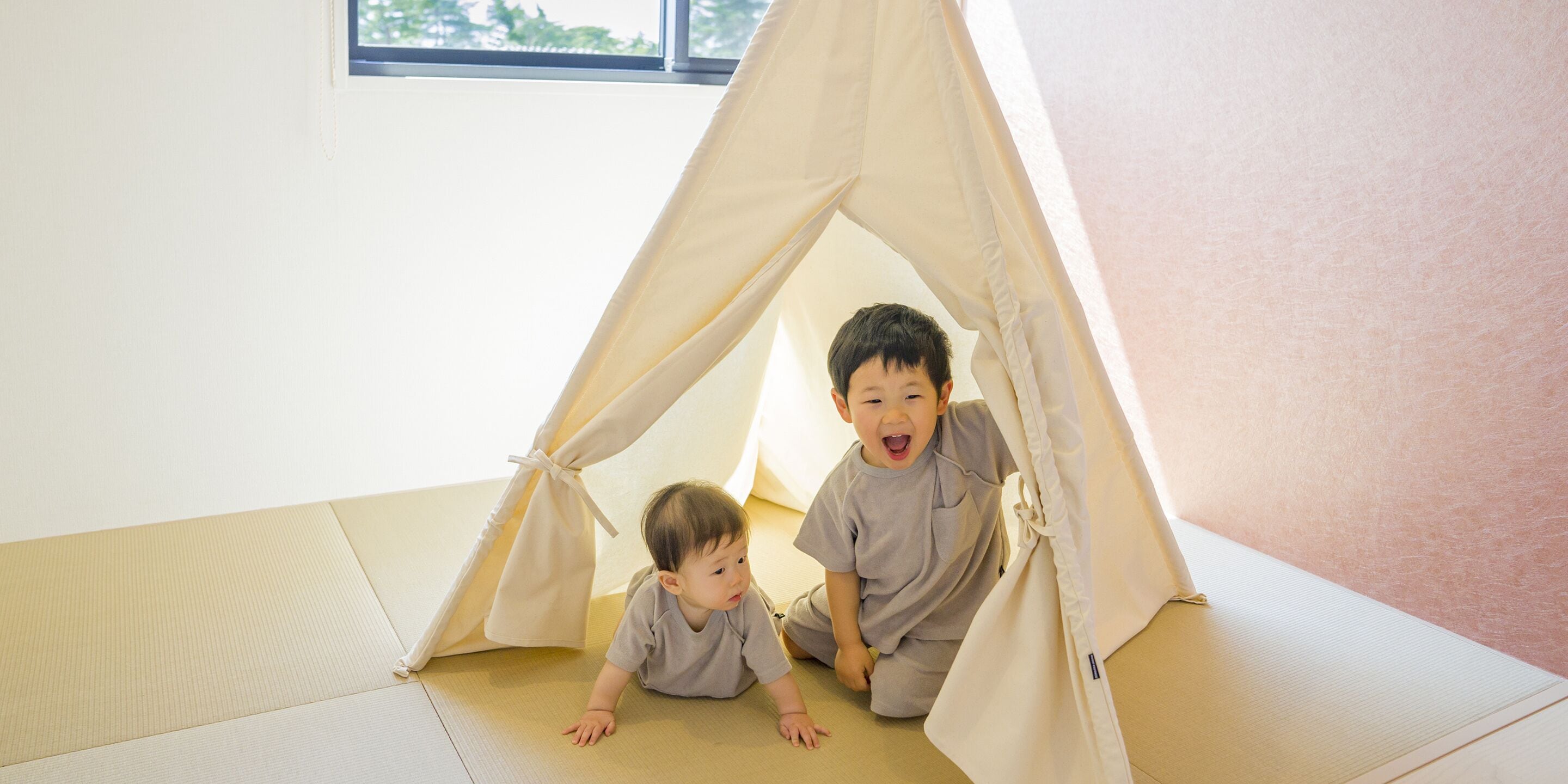 Two children in a tent-like play area with mats on the floor.