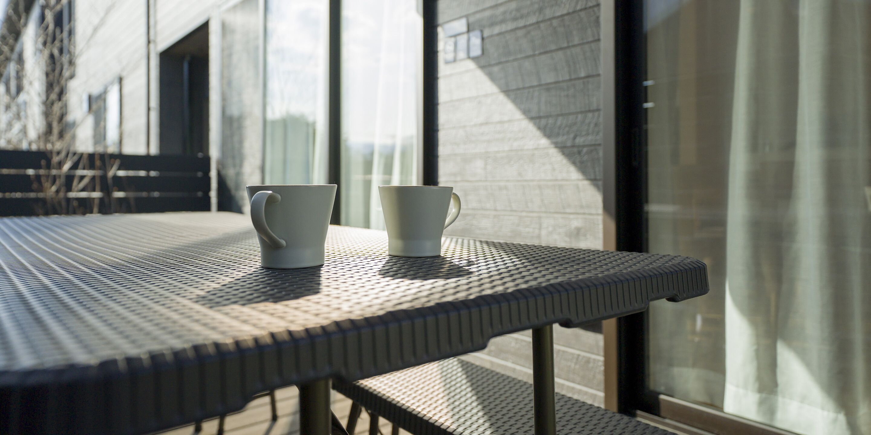 A table with two white cups and a window in the background.