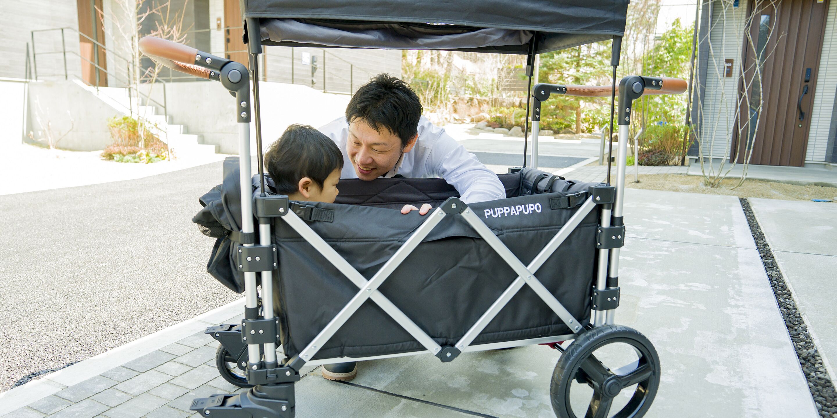 Ein Mann und ein Kind in einem PUPPAPUO Kinderwagen auf einem Bürgersteig.