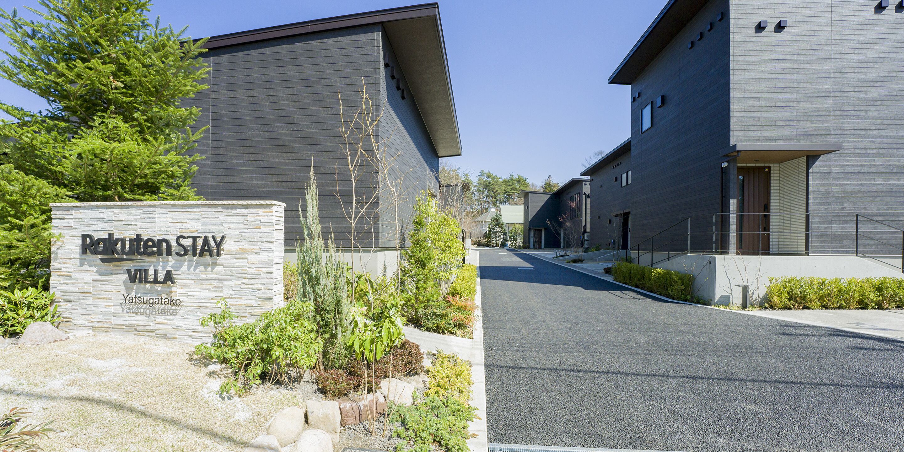 A modern building with a stone sign reading "Rakuten Stay Villa" and a well-maintained garden area.