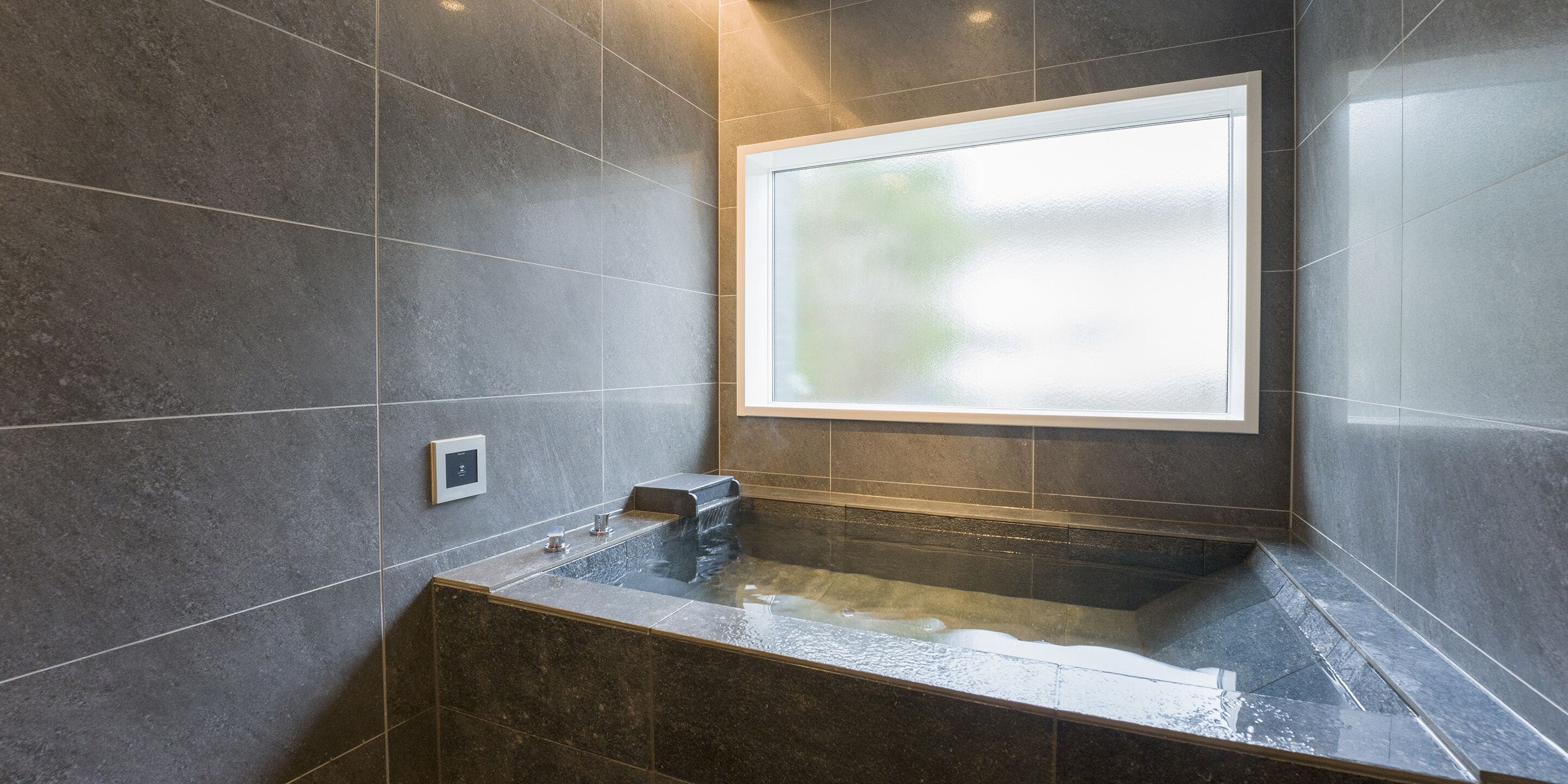 Une salle de bain moderne avec une grande baignoire, une fenêtre et un panneau de commande.