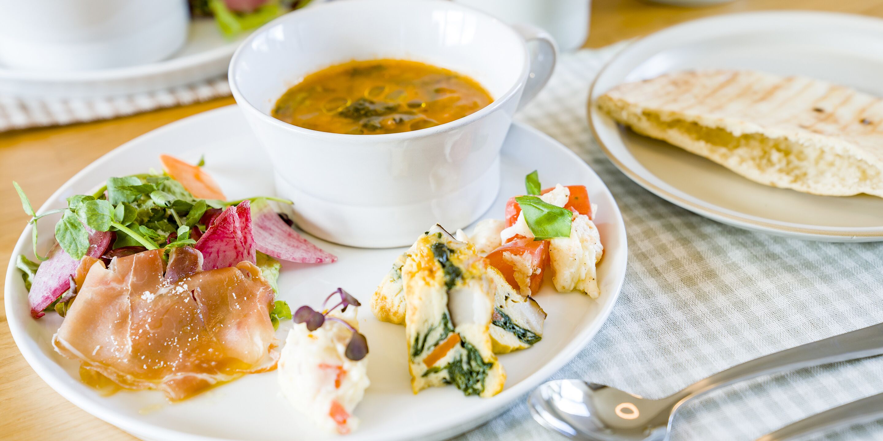 A plate of food with a bowl of soup, a slice of bread, and a salad.